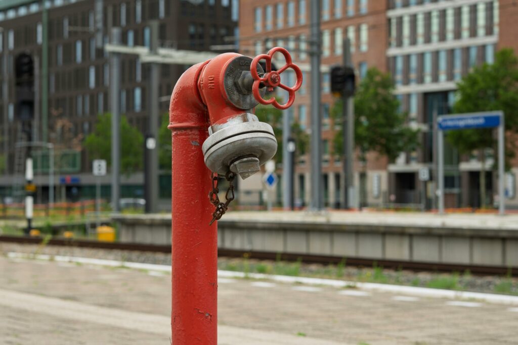 A red fire hydrant in focus with a blurred urban railway station in the background.